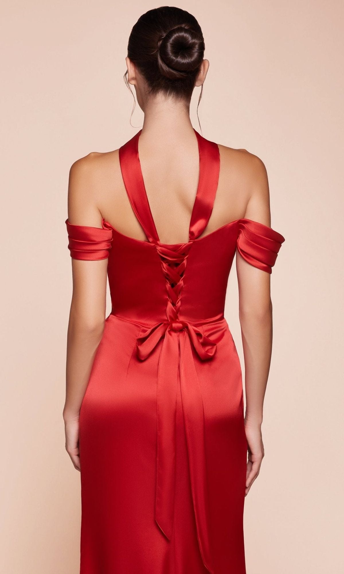A woman with dark hair in a bun is photographed from behind wearing the Lace-Up Off-Shoulder Prom Dress: Ladivine 7452, a red satin gown with crisscross lace-up back detailing and a bow.